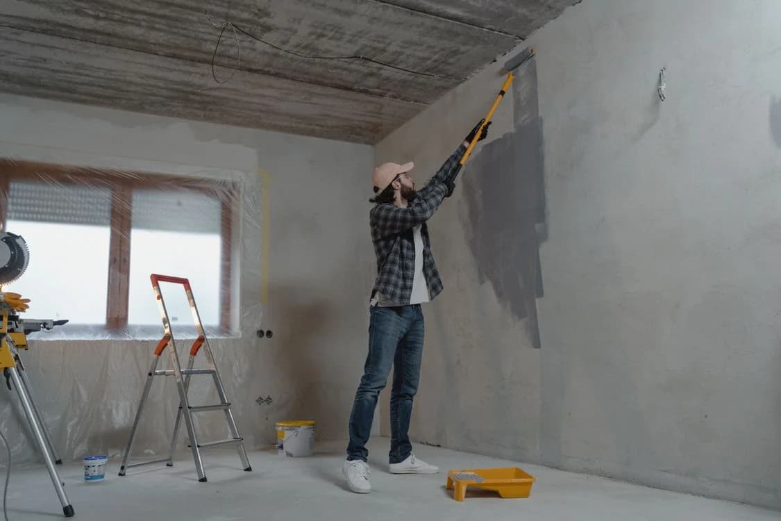 Målare som målar taket med roller i ett rum under renovering.